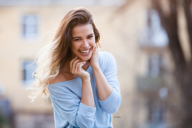 Young woman in blue sweater smiling and laughing outside.