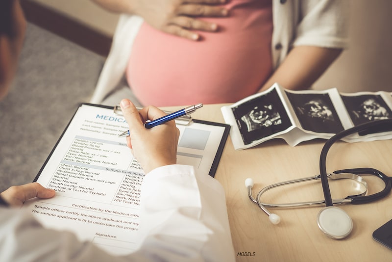 Pregnant women wearing pink with only belly showing at gynecologist's office.